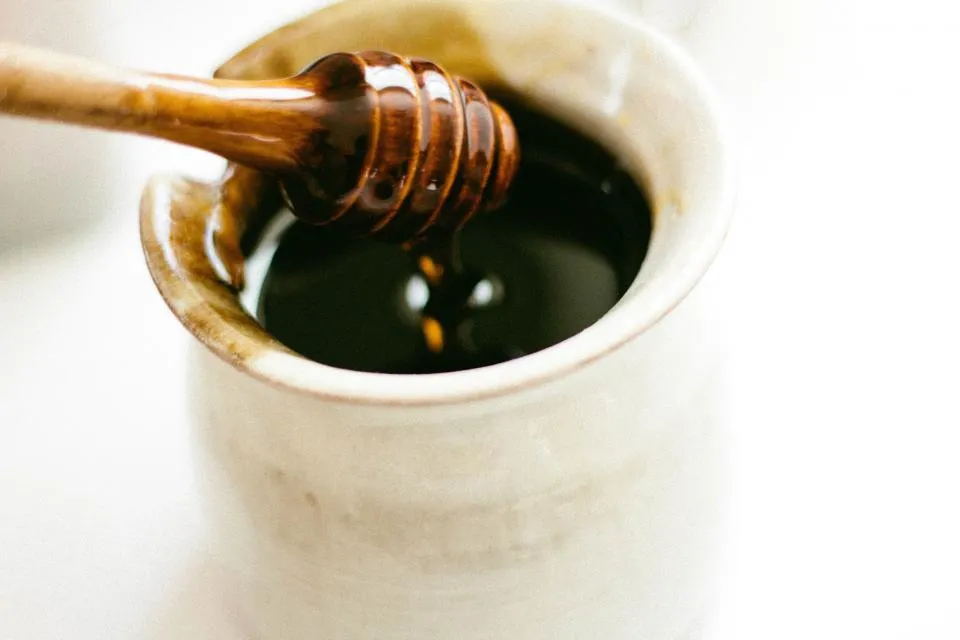 Wooden dipper resting in a ceramic pot of dark coconut syrup